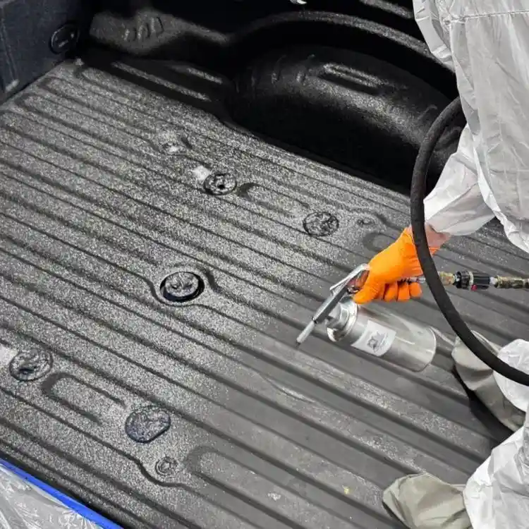 Close-up of a spray gun applying Flak Jacket PRO for a professional, textured bedliner finish